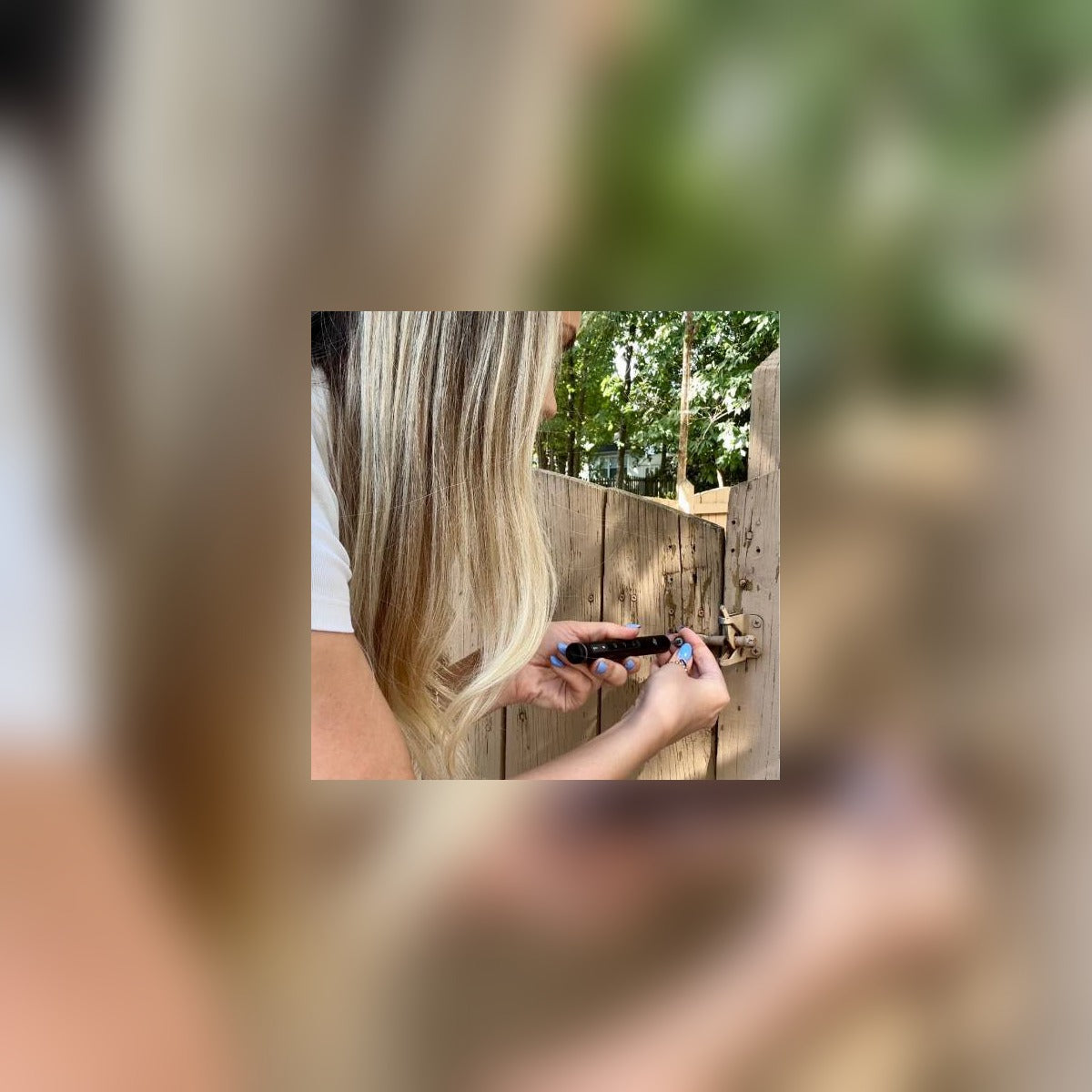 Woman using the pen driver on a small screw at a backyard fence
