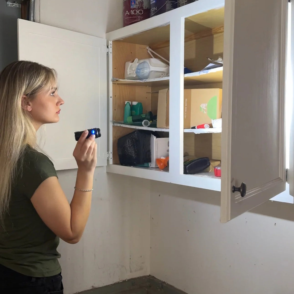 Woman using the Tactical Flashlight to look into a garage cupboard