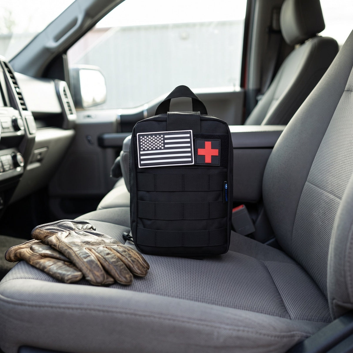 Trauma First Aid Kit on the passenger seat of a pickup truck next to work gloves
