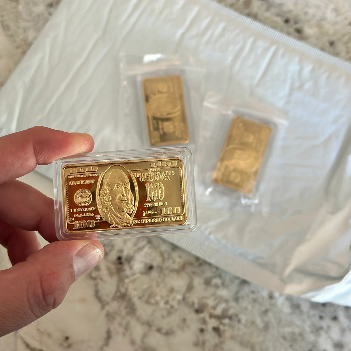 Ben Franklin $100 gold-plated bar sealed in a clear protective capsule, held in hand