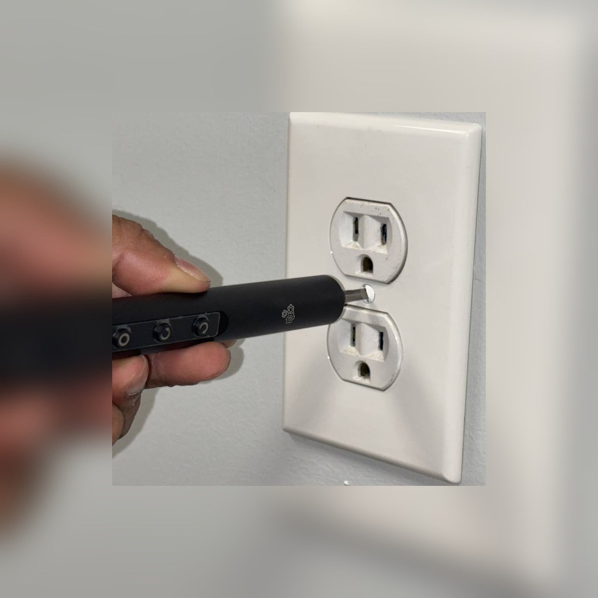 Hand using the electric pen driver on a wall outlet screw