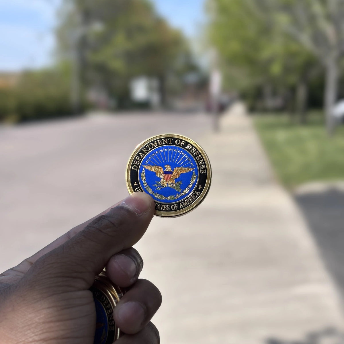 Defense Tribute Coin held between two fingers outdoors to show its size