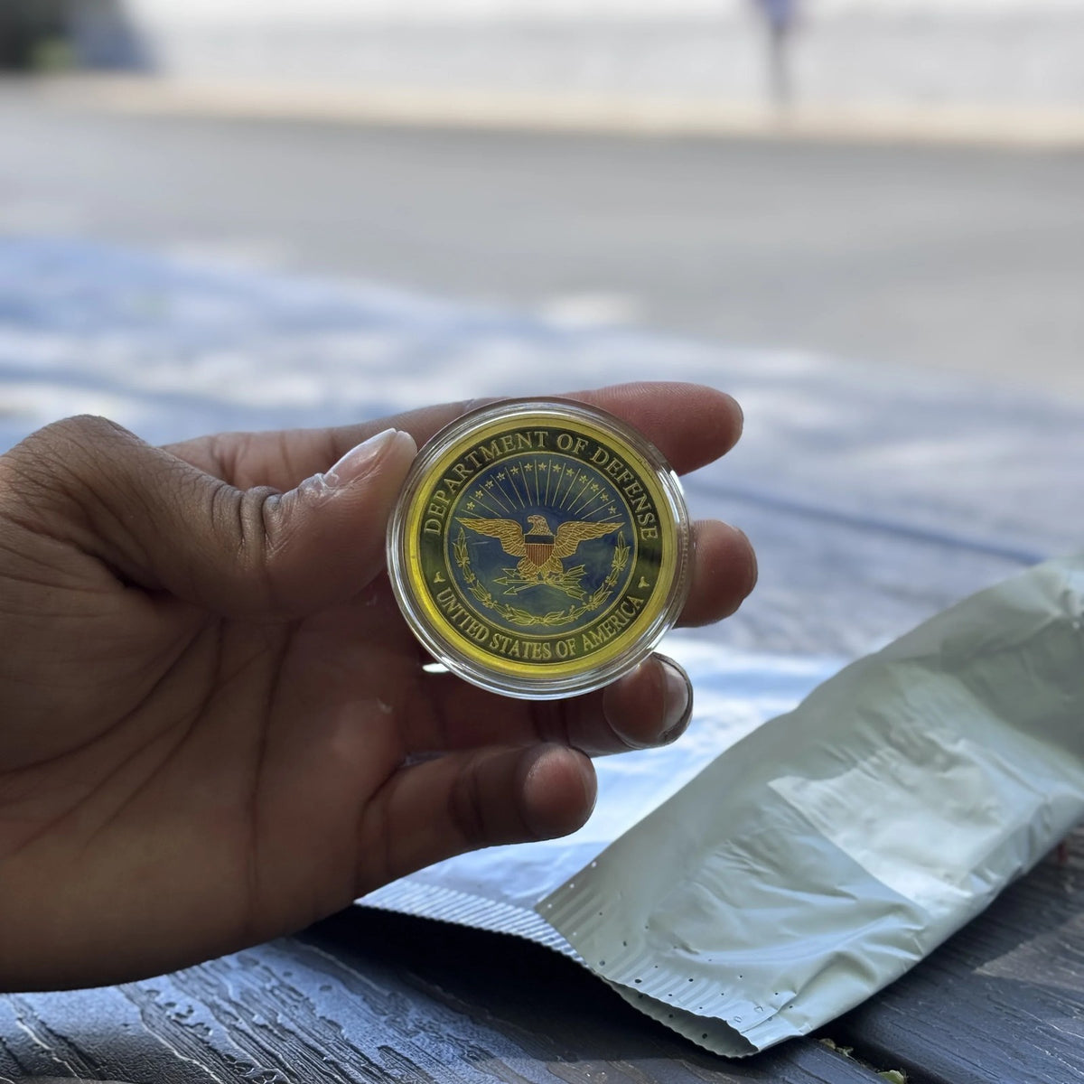 Defense Tribute Coin in its clear capsule, eagle side, held in hand