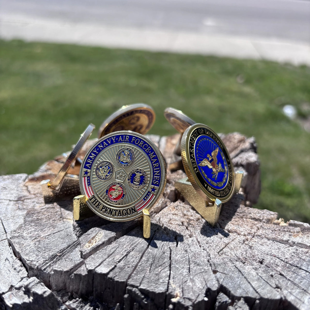 Defense Tribute Coins displayed on small stands on a tree stump, both sides showing