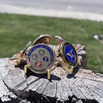 Defense Tribute Coins displayed on small stands on a tree stump, both sides showing