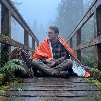 Man sitting on a foggy footbridge with the Emergency Sleeping Bag around his shoulders