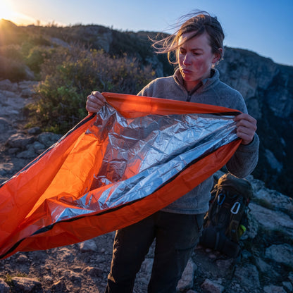 Woman unrolling the Emergency Sleeping Bag on a rocky ridge