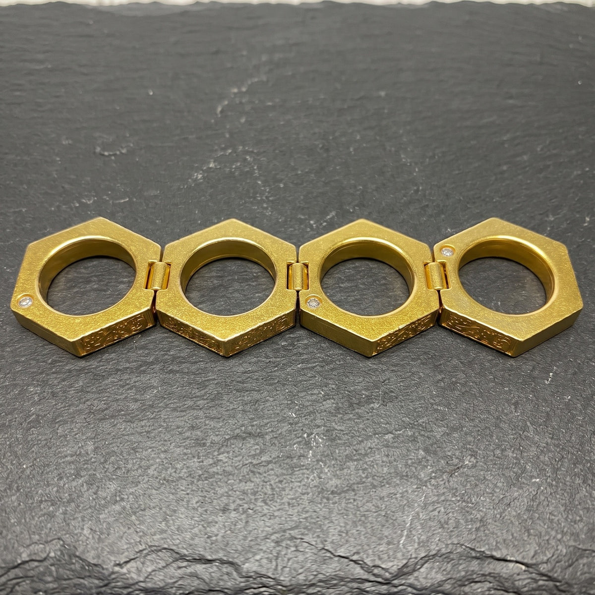 Knuckle Ring opened flat into a row of four hexagonal rings on slate
