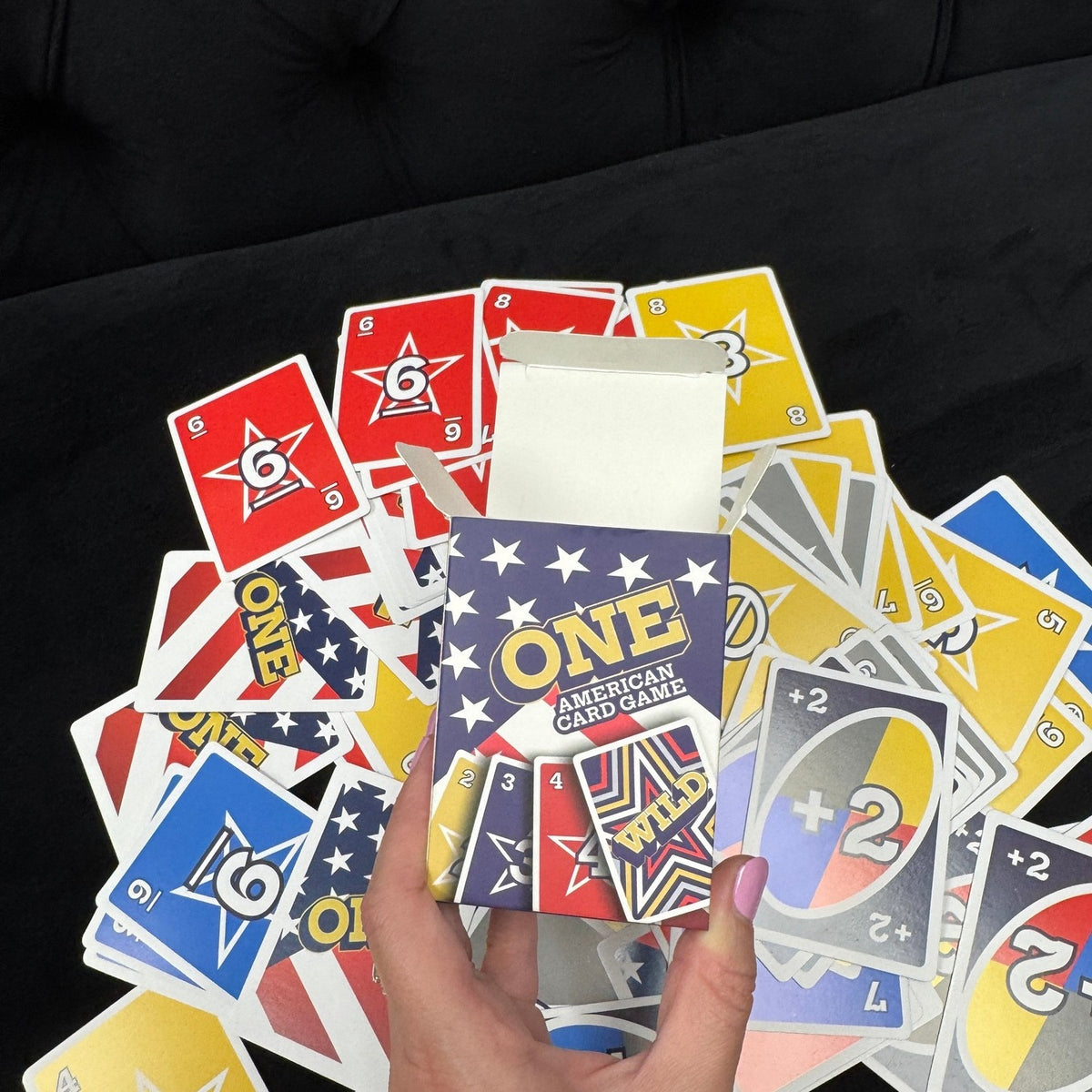 ONE American Card Game box opened with cards spread on a black couch