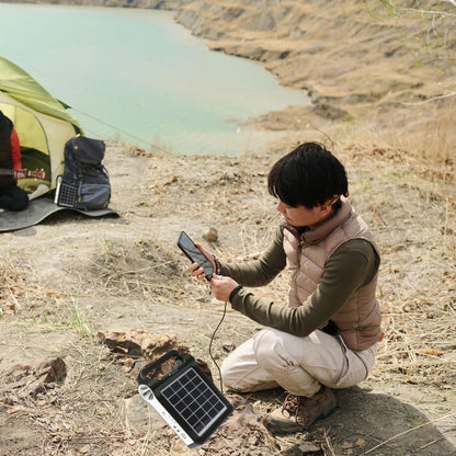 Camper charging a phone from the Portable Power Station beside a lake