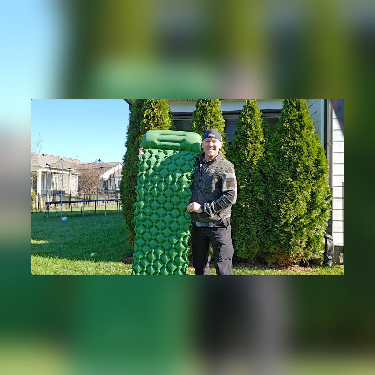 Man standing beside the inflated Survival Mattress held upright in a backyard