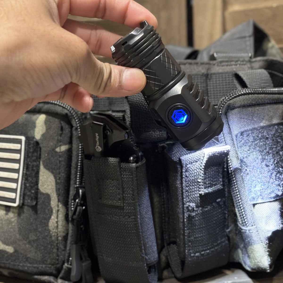 Tactical Flashlight lit and held above a camo MOLLE pouch with a flag patch