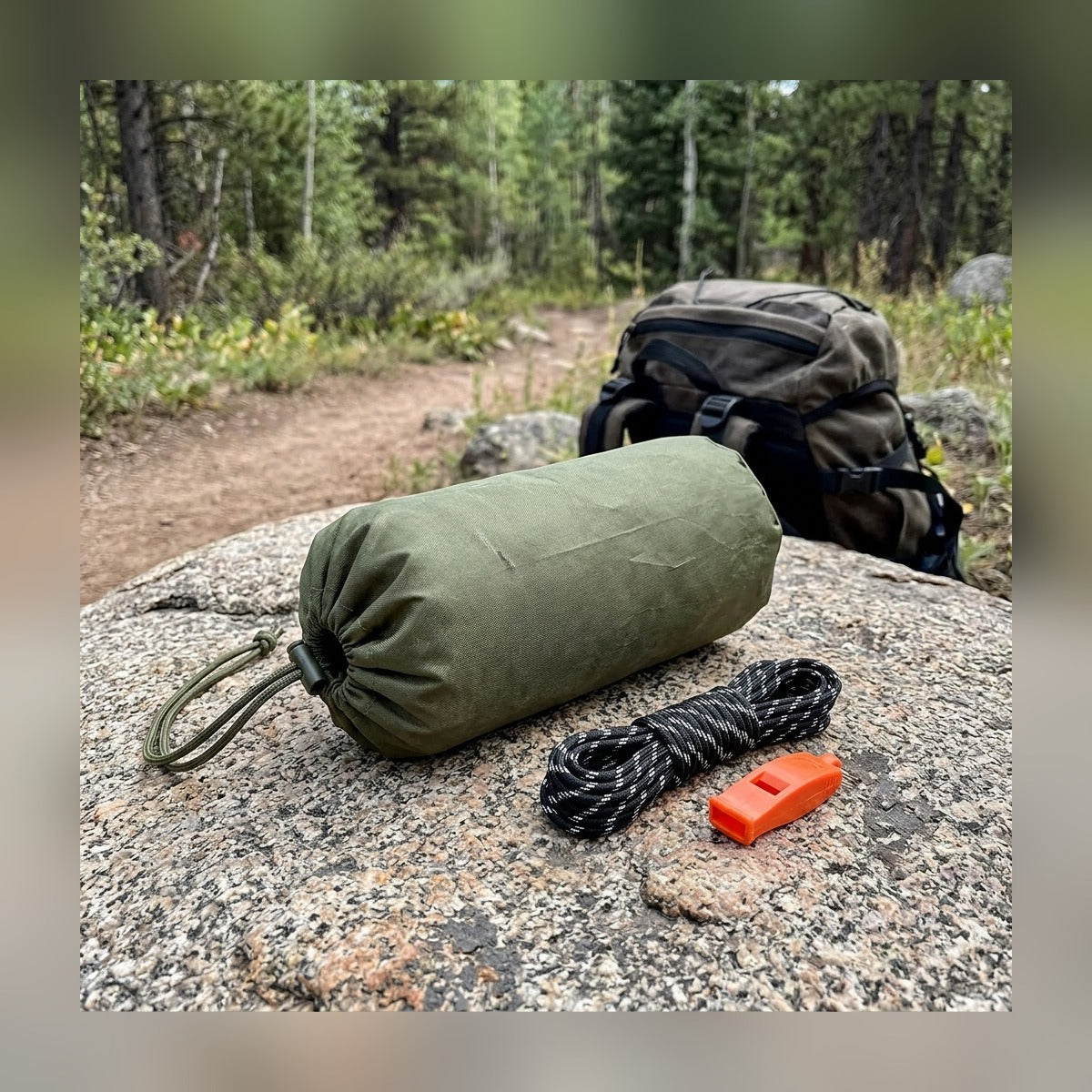 Emergency Tube Tent kit laid out on a rock: stuff sack, paracord and whistle