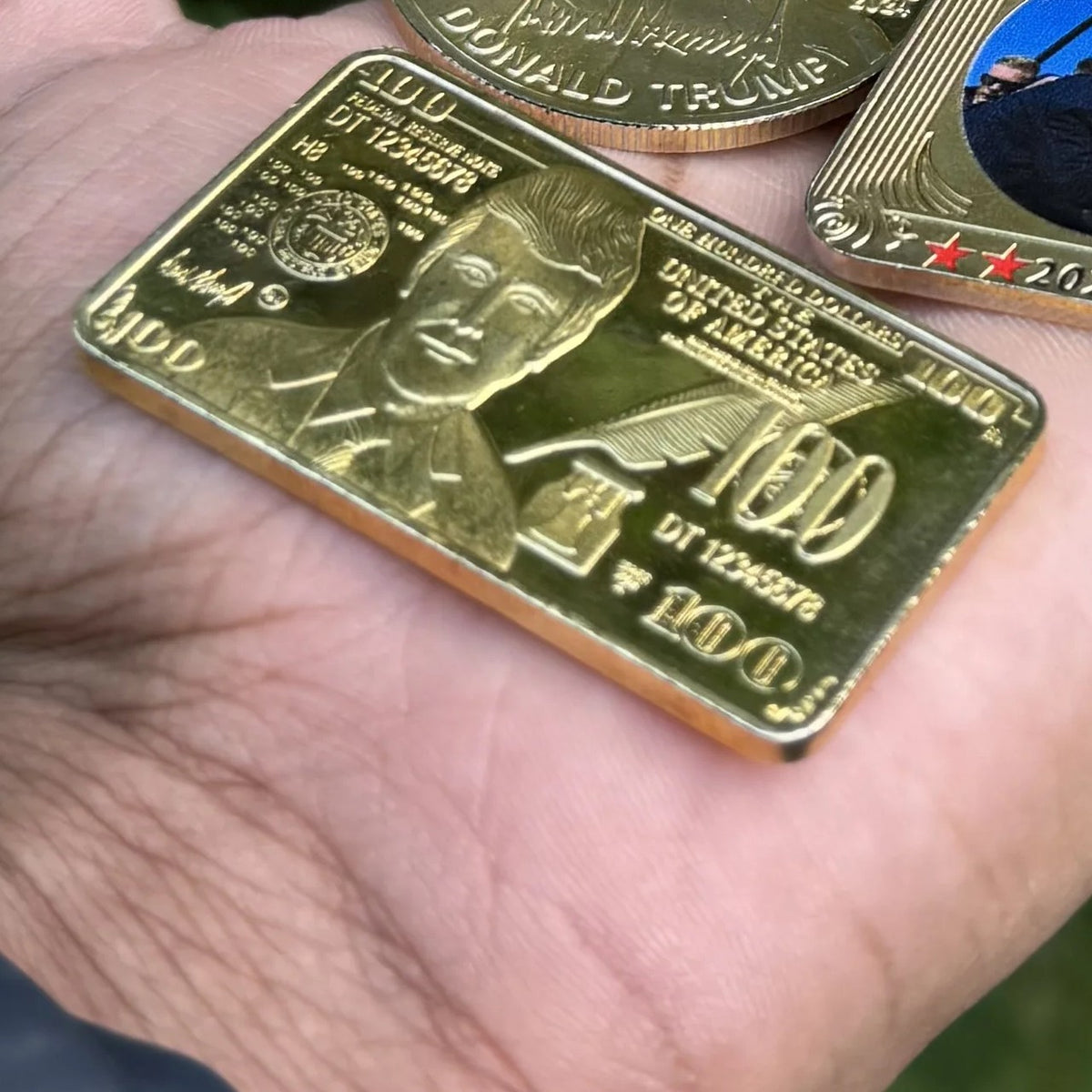 Trump $100 portrait gold-plated bar resting in an open palm for size