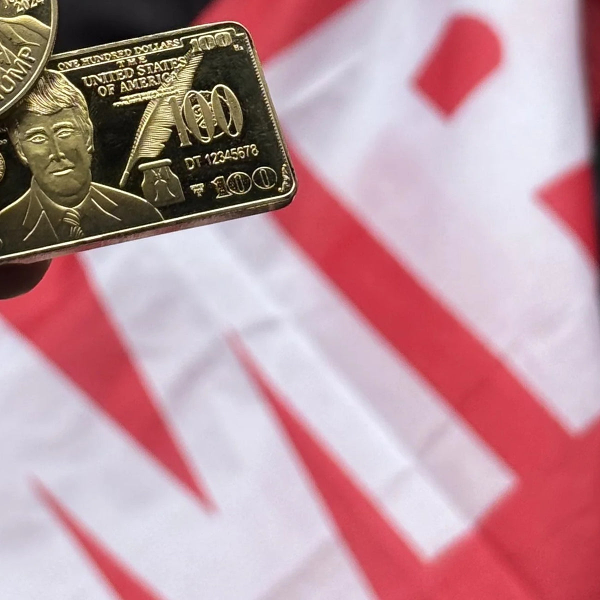 Trump $100 portrait gold-plated bar held outdoors next to a Trump flag