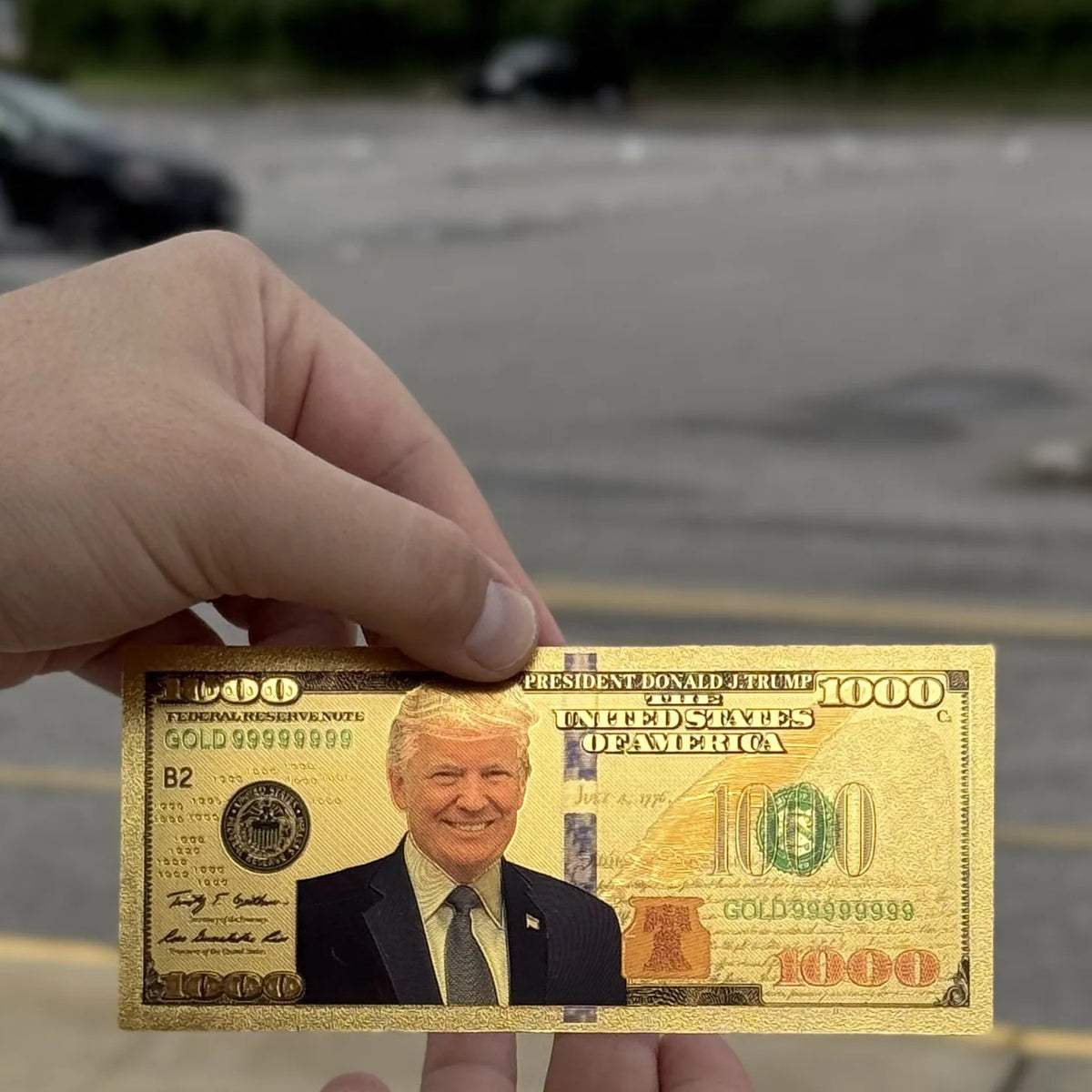 Trump $1000 gold foil novelty bill held up outdoors on a cloudy day
