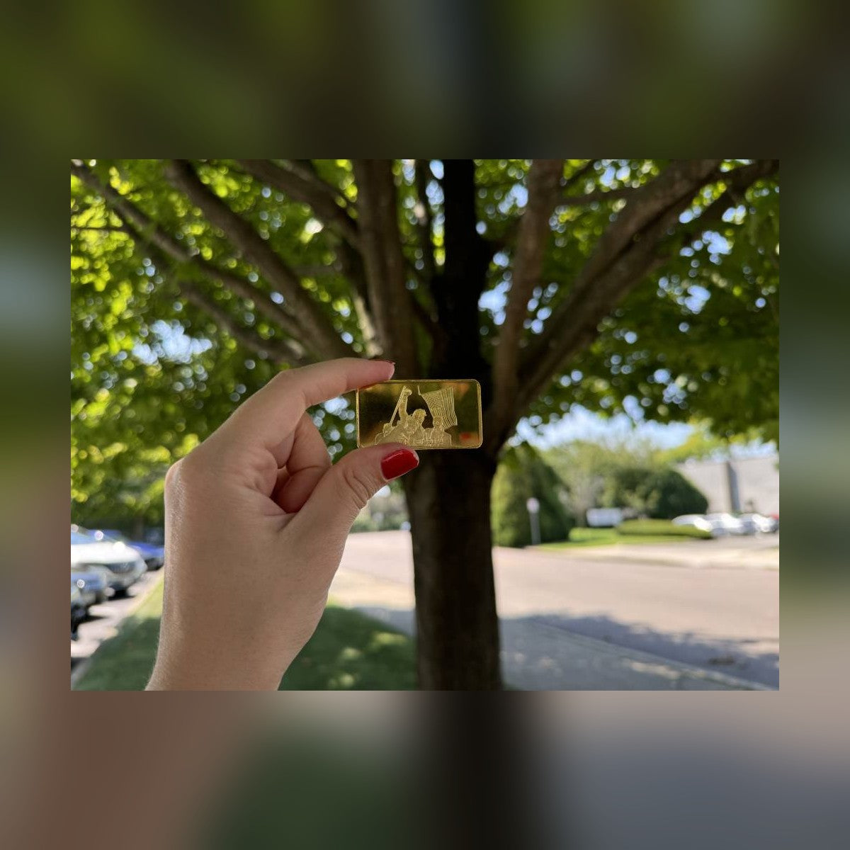 Trump July 13 commemorative gold-plated bar held between fingers outdoors for size