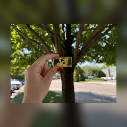 Trump July 13 commemorative gold-plated bar held between fingers outdoors for size