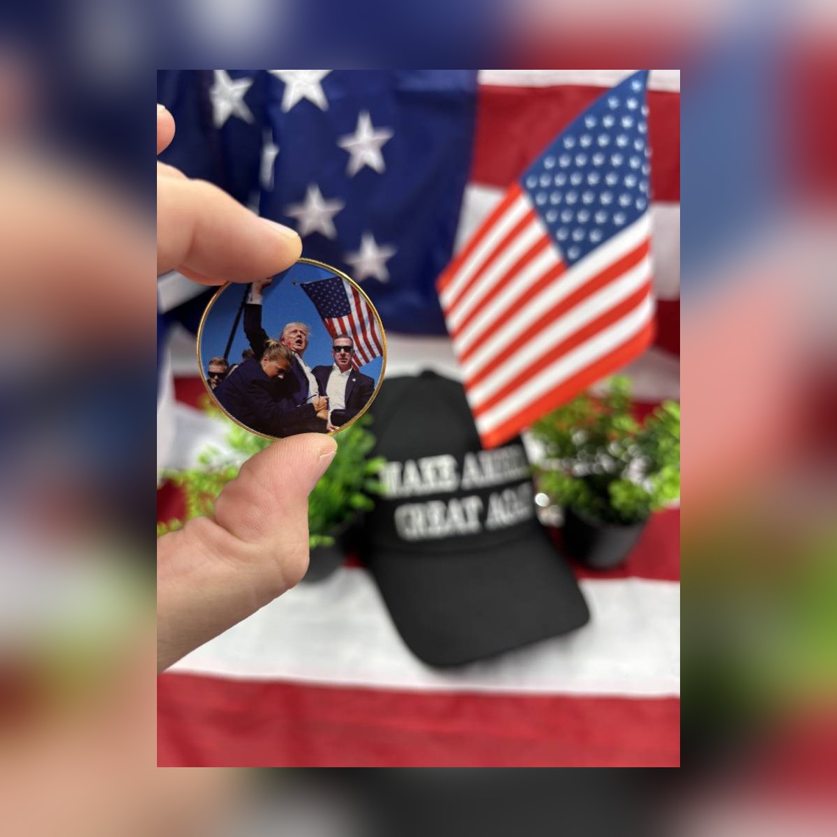 Trump July 13 Coin held between fingers in front of a flag and a MAGA cap
