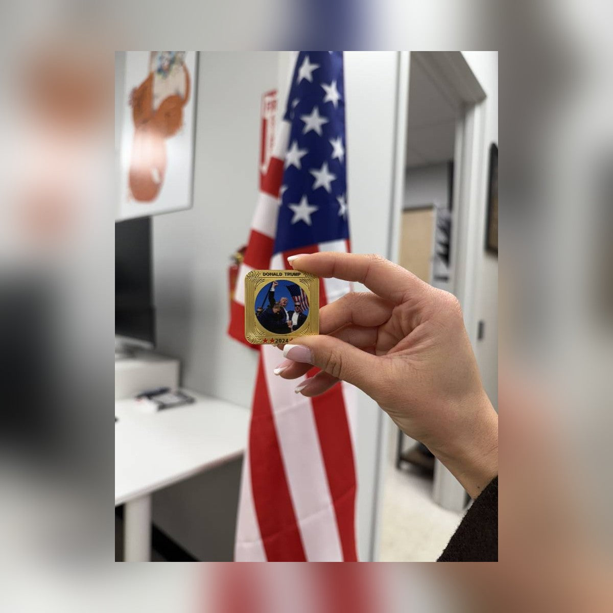 Trump July 13 Square Coin held between fingers beside a flag to show its size