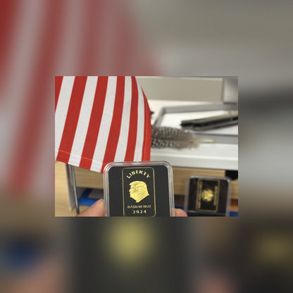 Trump Liberty 2024 black and gold bar held up at a desk beside a small American flag