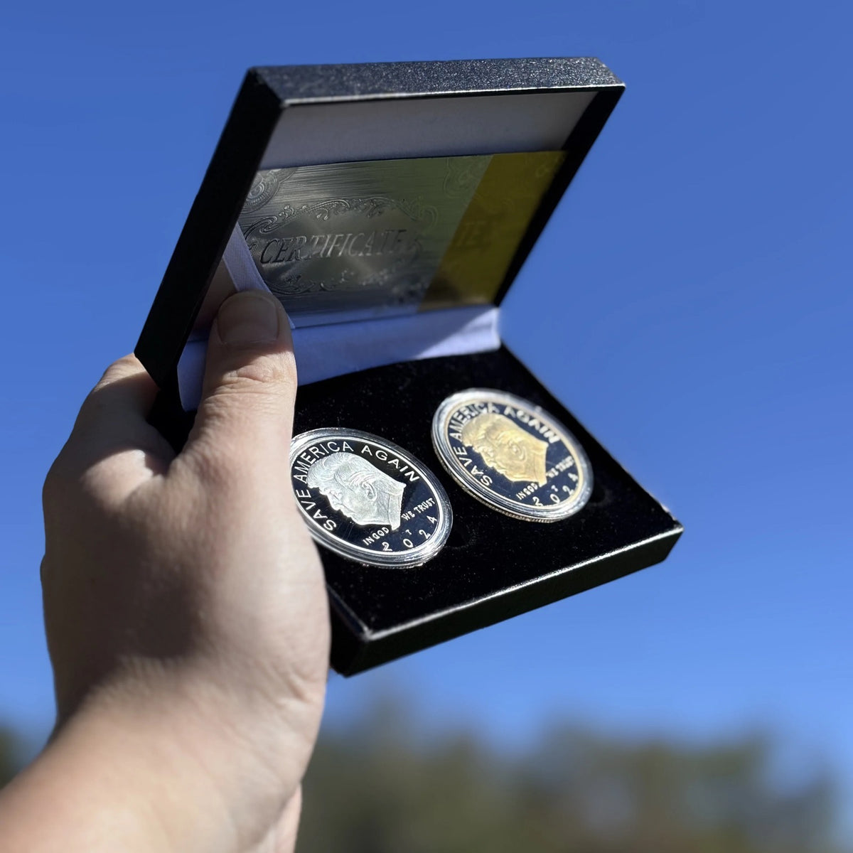 Trump gold and silver coin case held up against a blue sky