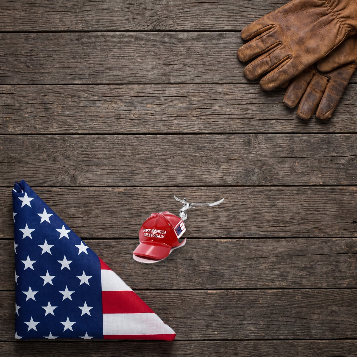 Trump MAGA Hat Keychain on a dark wood table beside a folded American flag