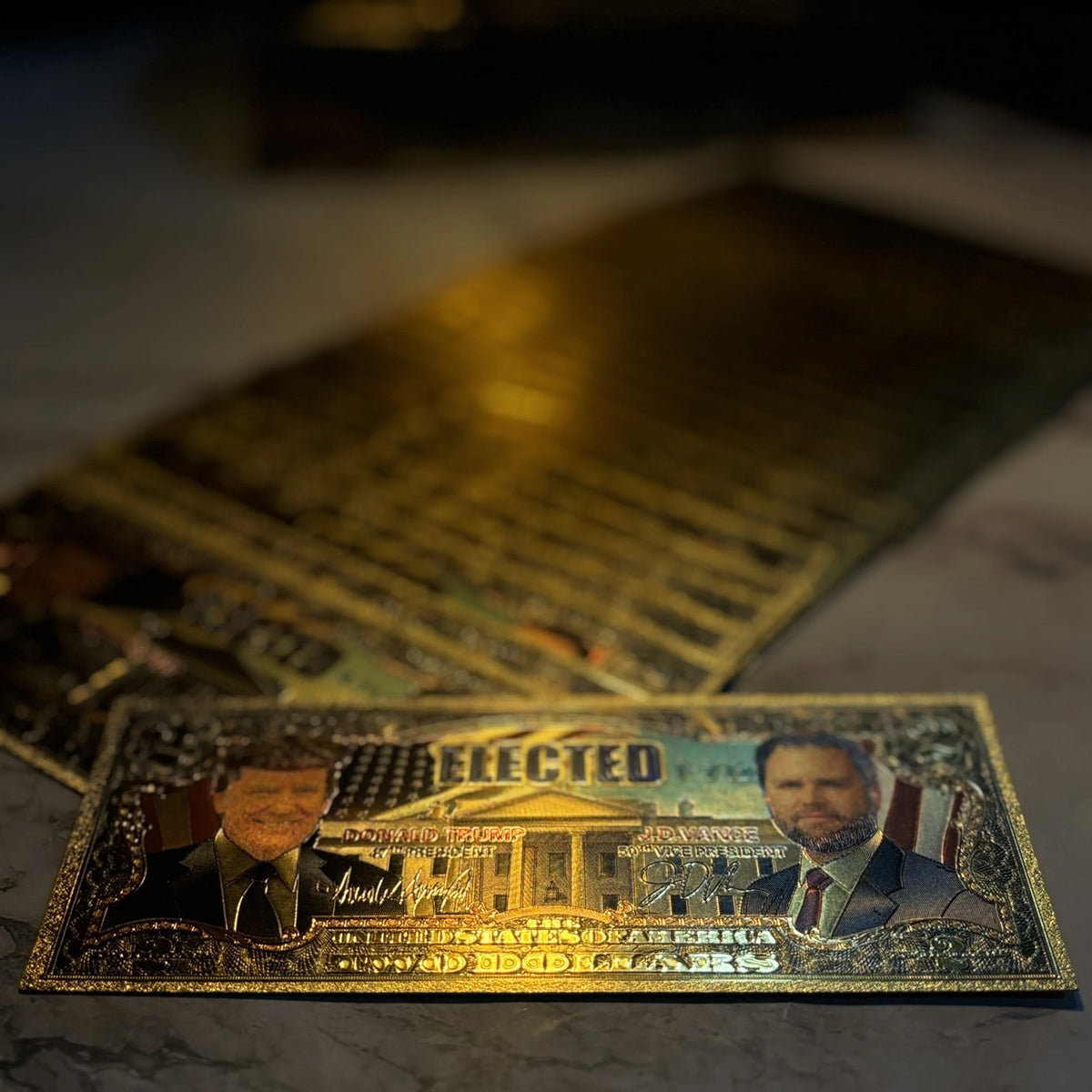 Trump Vance $2 gold foil novelty bill on a dark desk