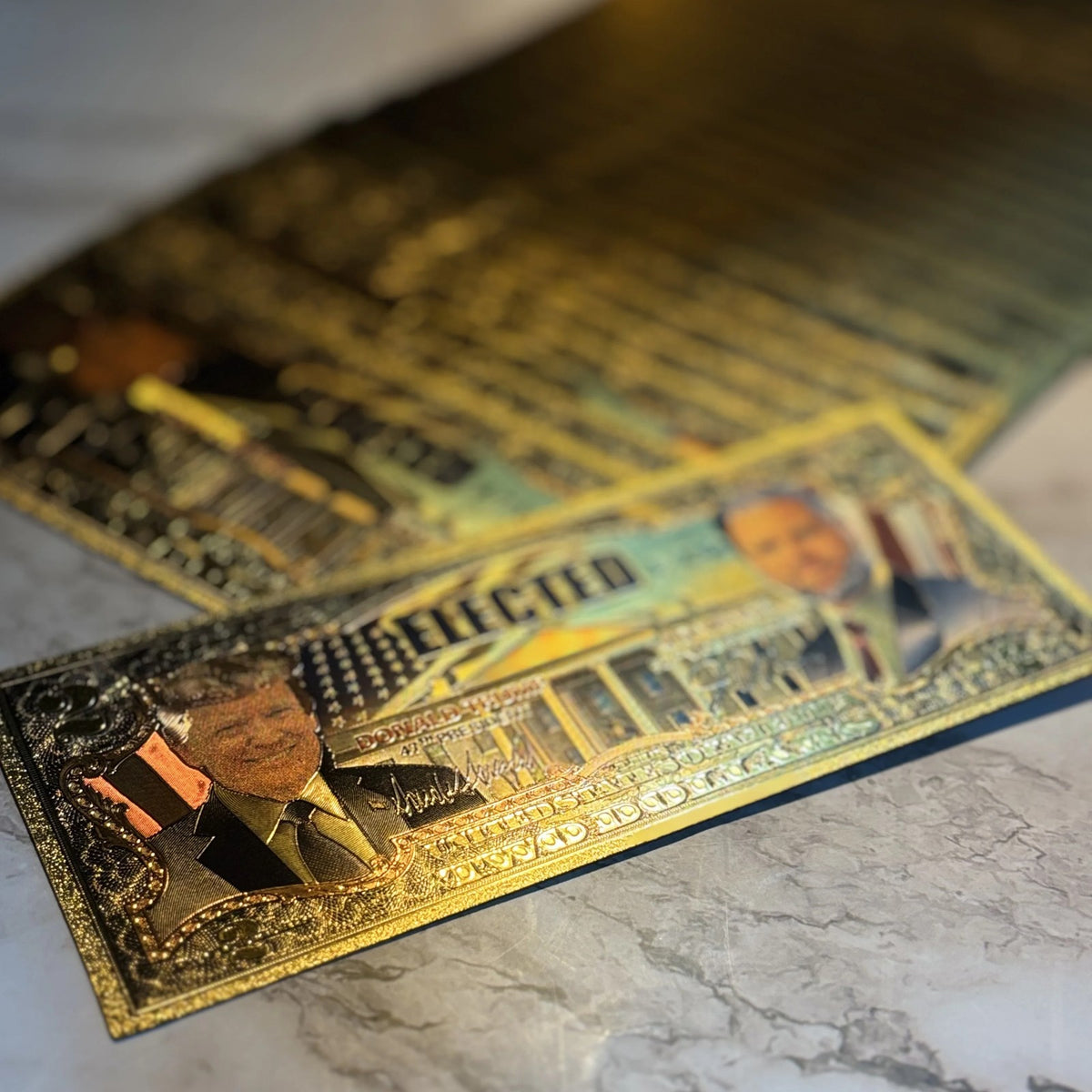 Trump Vance $2 gold foil novelty bills on a marble surface, angled view
