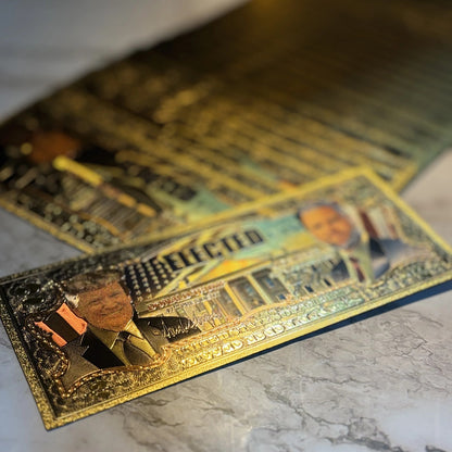 Trump Vance $2 gold foil novelty bills on a marble surface, angled view